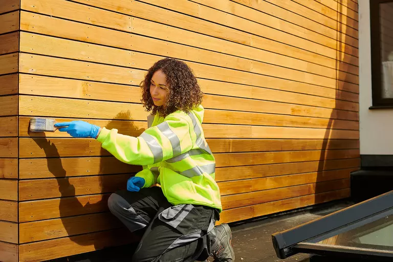 Woman staining the exterior of a home with wood siding.