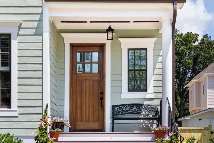 Black bench and potted plants on the front porch of a home with a wood entry door.