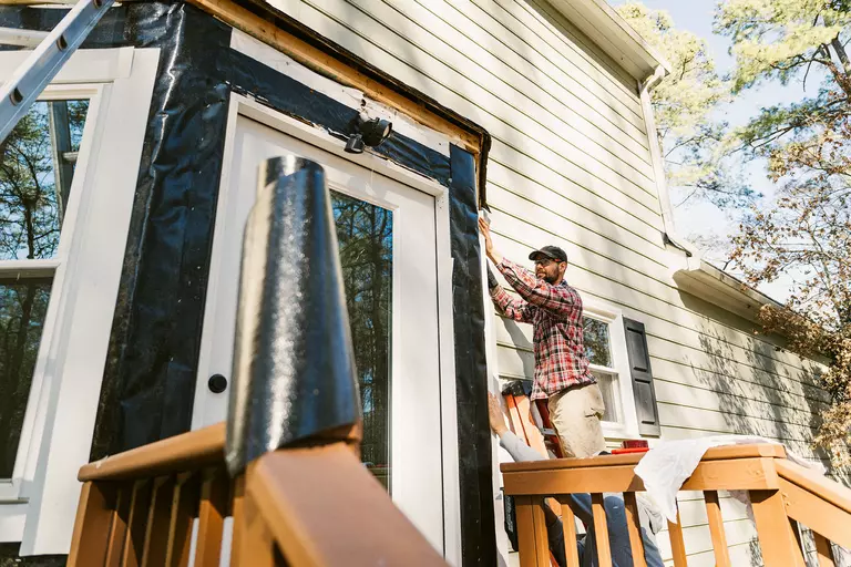 A man replacing the layer underneath a home’s vinyl siding around the back door.