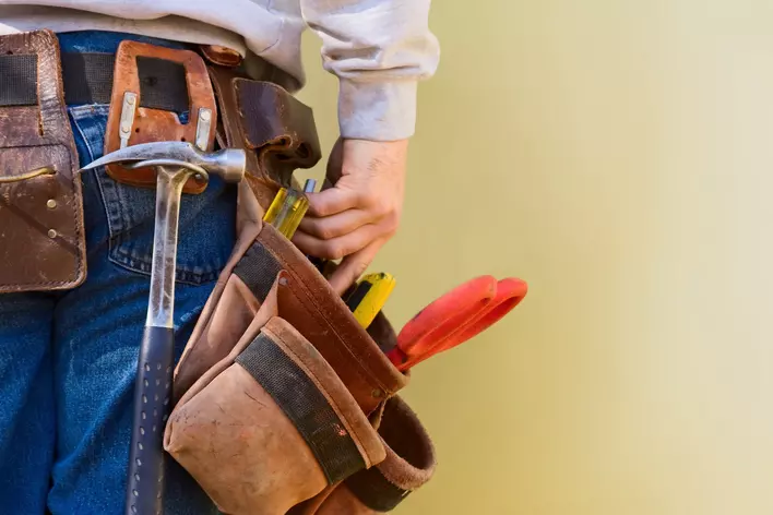 A toolbelt around a man’s waist that is equipped with a hammer, scissors, screwdrivers, and more.