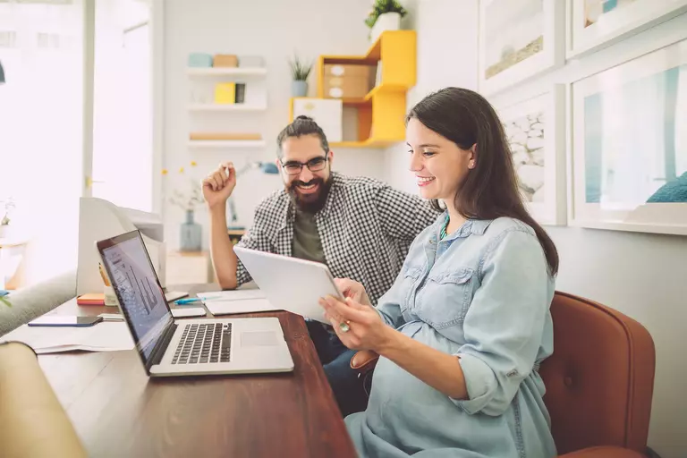 A woman and man reviewing documents and information on a laptop together.