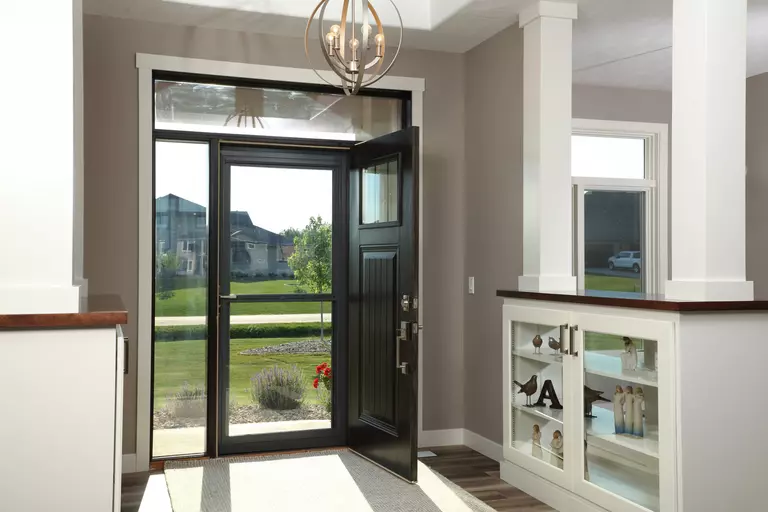 A full-view storm door pictured from within a home. The entry door is open; the storm door is allowing natural light to enter the foyer.