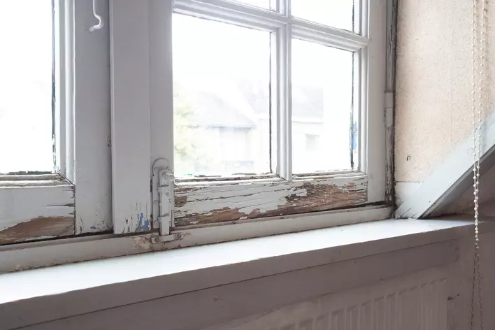 A white wooden window frame that is chipped, cracked, and has pieces breaking off it.