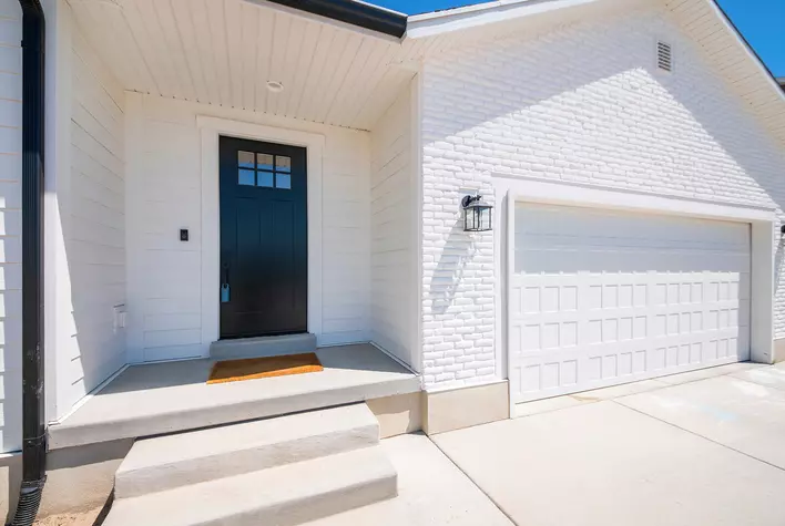 White brick exterior of a home with a black door and orange doormat