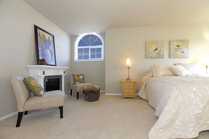 Large bedroom with white bed and fireplace with custom architectural shape windows and sliding windows.