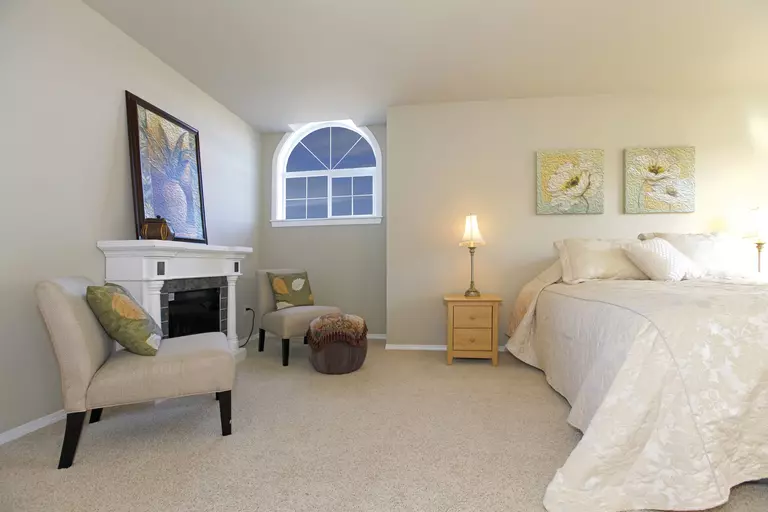 A large bedroom in the basement of a home that is naturally lit by an architectural-shaped window. 