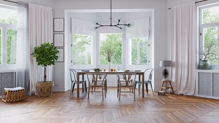 A large dining area with a bay window with shades and a pair of casement windows to either side.