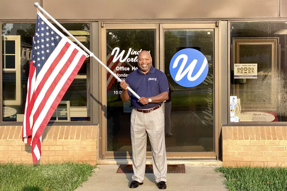 A Window World owner holding a flag in front his store