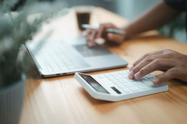 A person using a calculator and a laptop computer on a desk