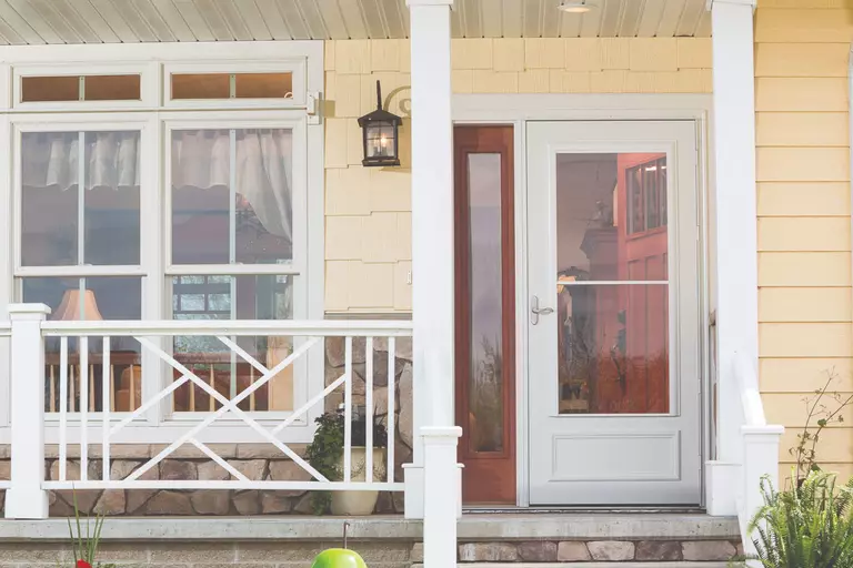 White storm door over a woodgrain entry door with a sidelite.