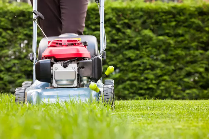 A homeowner mowing the lawn with a push lawnmower to help increase curb appeal.