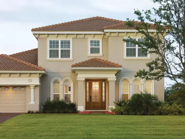 A large tan house with a lawn and trees as well as a brown energy-efficient front door at the home’s entrance.