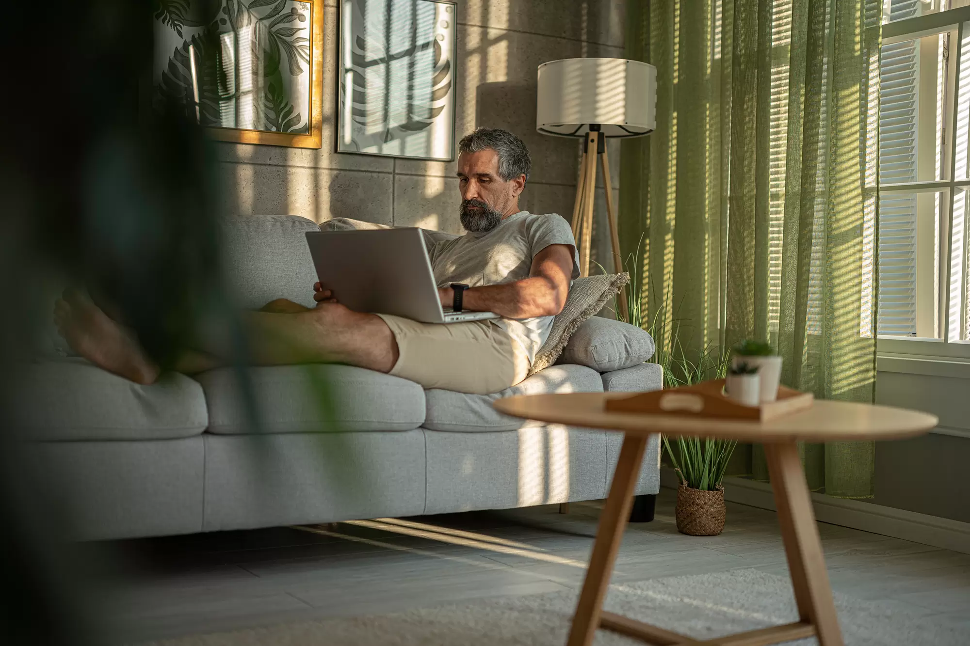 Man seated across a living room couch using a laptop.