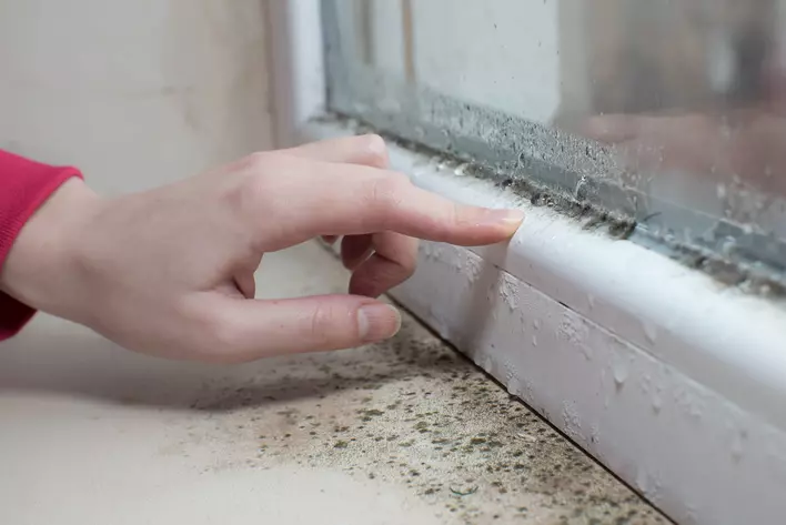 A person touches the bottom of foggy windows as condensation builds at the bottom of
            the pane of glass.