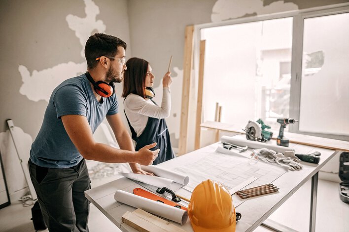A couple planning out their DIY home remodel project surrounded by construction tools and materials.