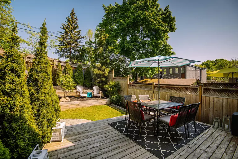A set of outdoor chairs and a glass-topped table sit atop a rug in an outdoor living space.