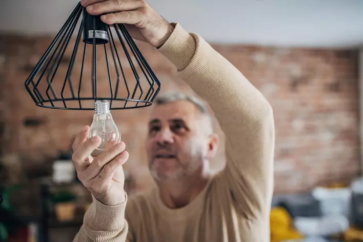 A man carefully puts a new lightbulb into a new ceiling-mounted light fixture.