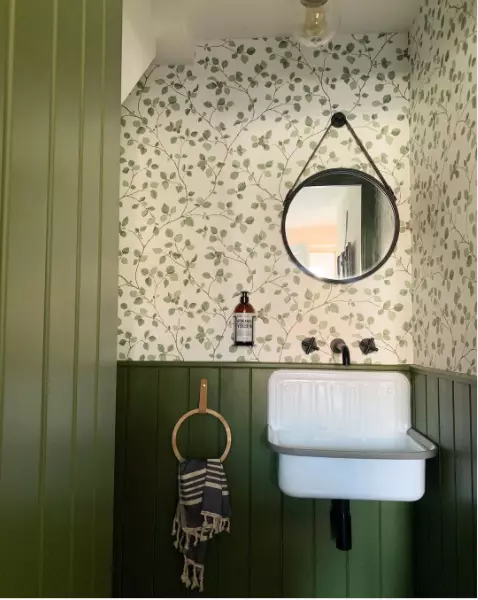 A unique green bathroom with stylish wallpaper and a circular mirror