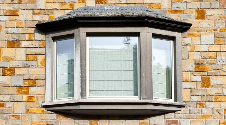 The stone exterior of a building with a bay window and curtains viewed from outside.
