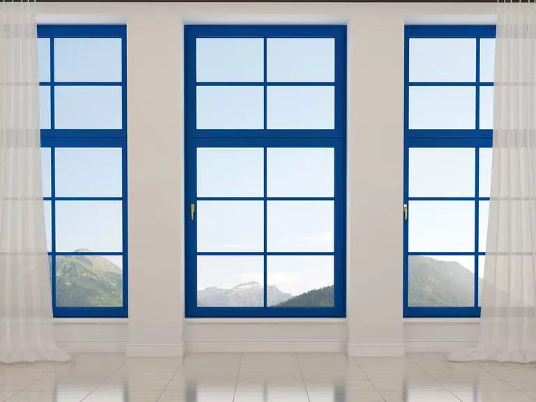 A trio of tall vertical rectangular windows with blue frames and white curtains.