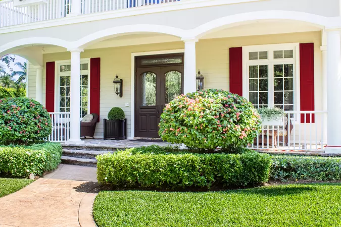 Red raised panel Colonial Shutters on a porch behind shrubs