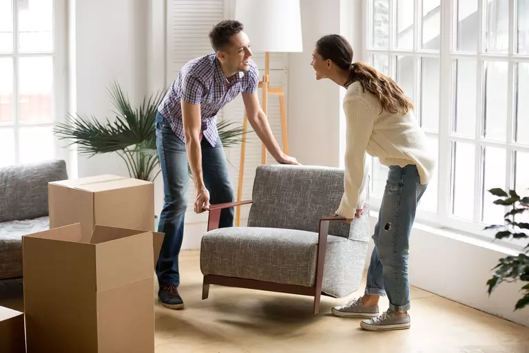 A man and woman setting down a chair in the living room.