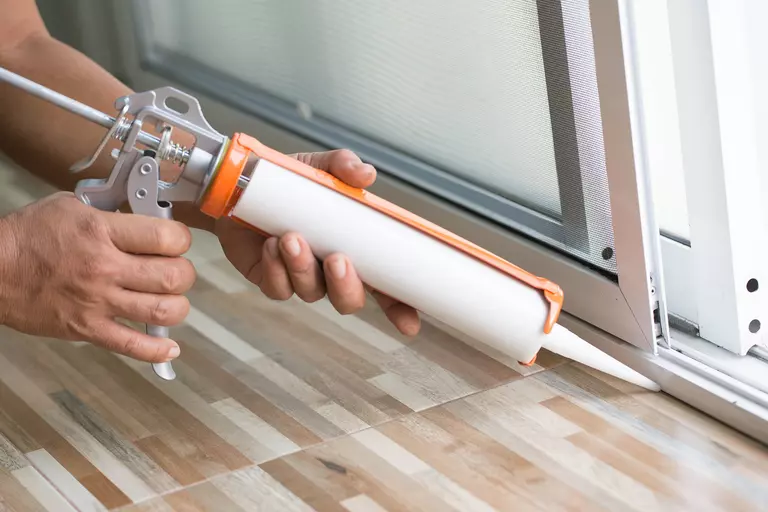 Worker with a caulk gun sealing the bottom edge of a sliding patio door.