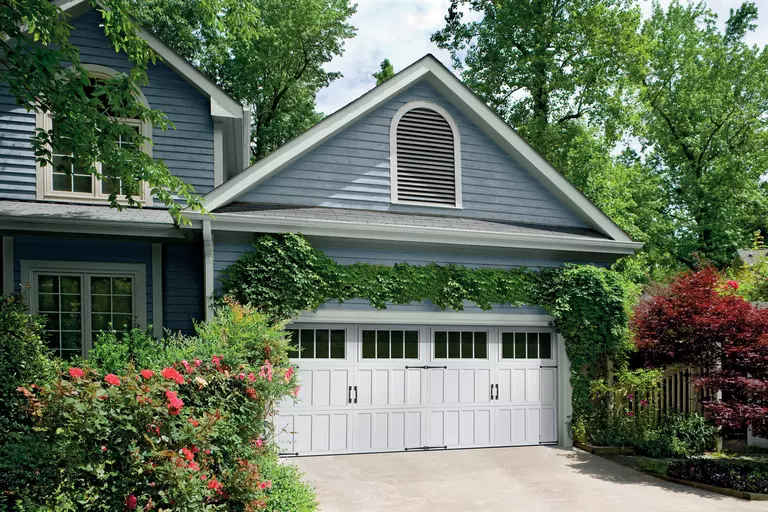 Front of a home with lush landscaping and carriage-style garage doors.