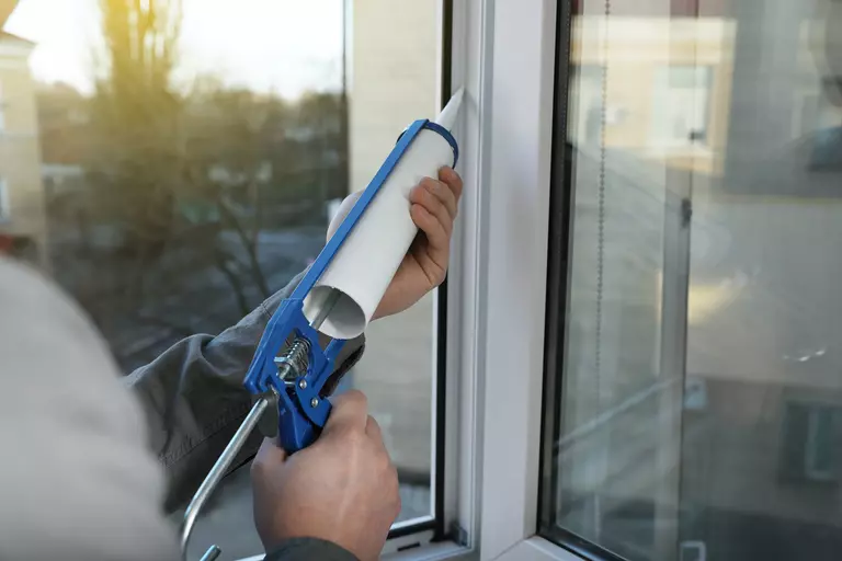 Worker using a caulk gun to seal the gaps around the edges of a window.