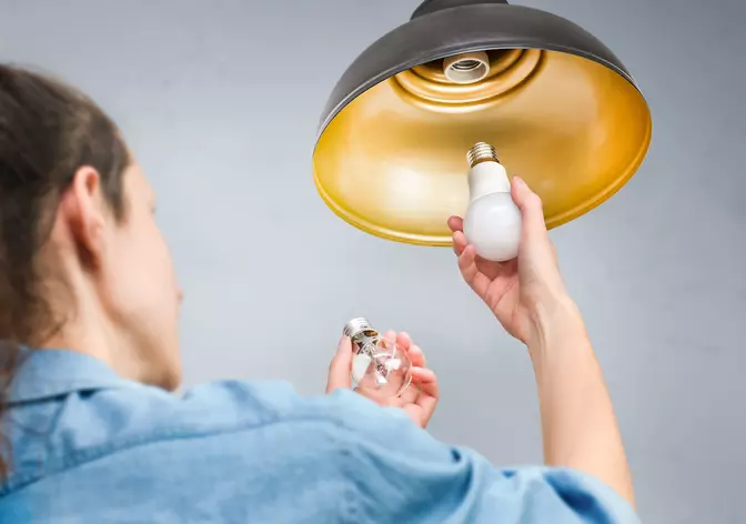 A woman swapping out her old light bulb with an energy-efficient LED bulb.