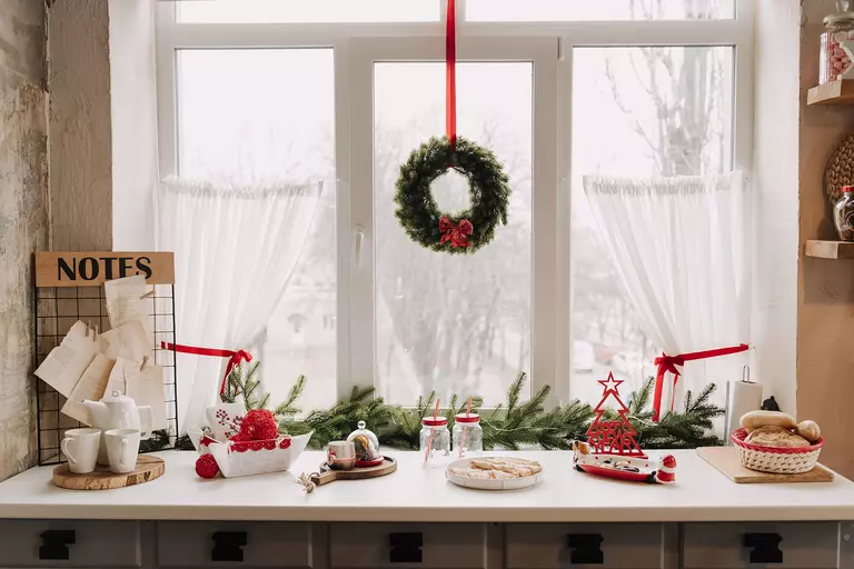 A wreath hanging from a ribbon in front of a casement window and a festively decorated shelf.