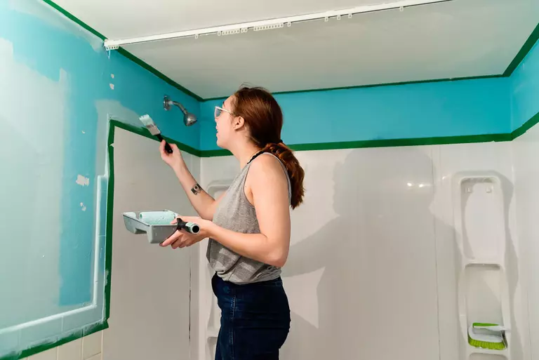 Woman painting her bathroom walls to better renovate her home.