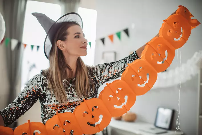 Woman dressed up for Halloween as she holds a hanging curtain to place on front door.
