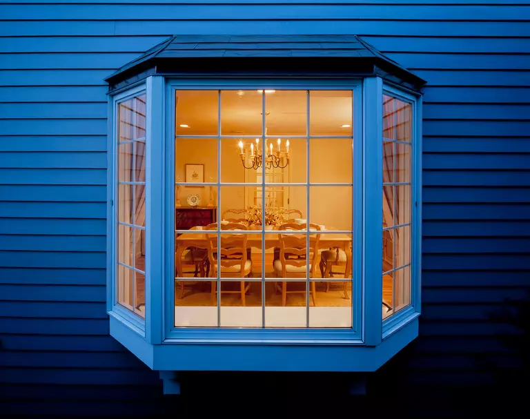 The outside of a dining room of a home with vinyl siding viewed through a bay window.