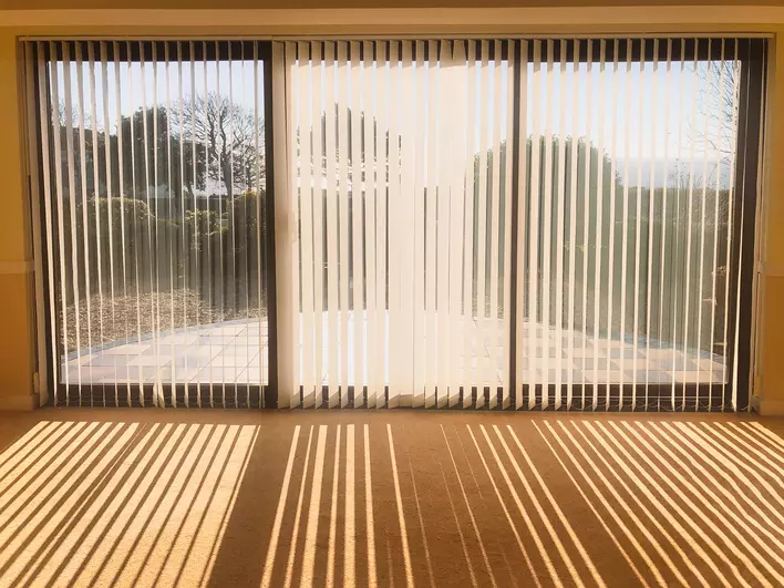 Light shining through vertical blinds as window treatments for patio doors in a home