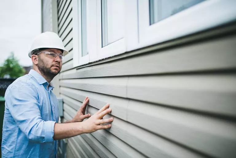 A contractor inspecting vinyl siding on a home to determine if repair or replacement is needed.