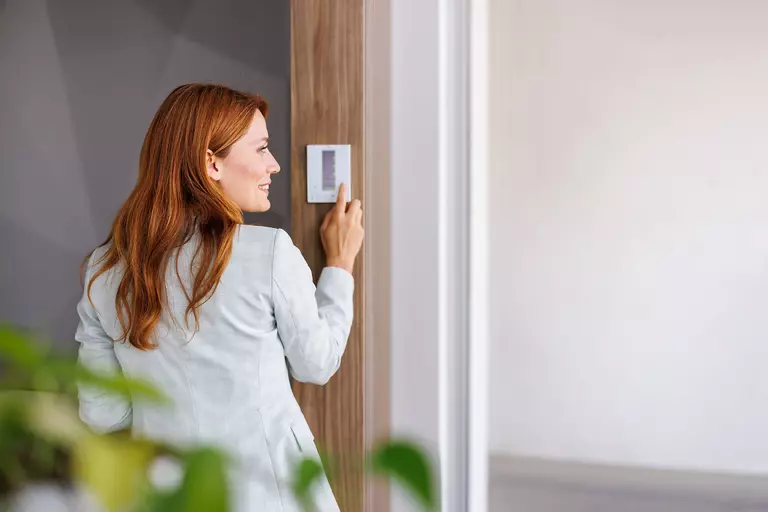 Woman adjusting thermostat.