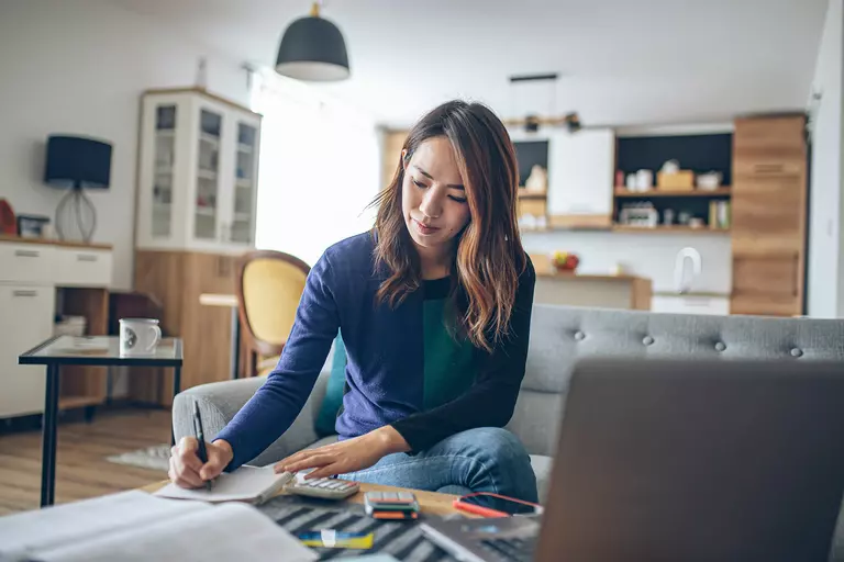Woman writing in a notebook with a laptop open.