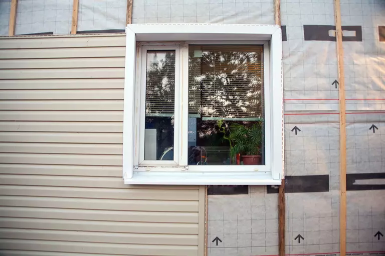 Tan-colored vinyl siding on a section of a home, with the adjacent section displaying the home frames.