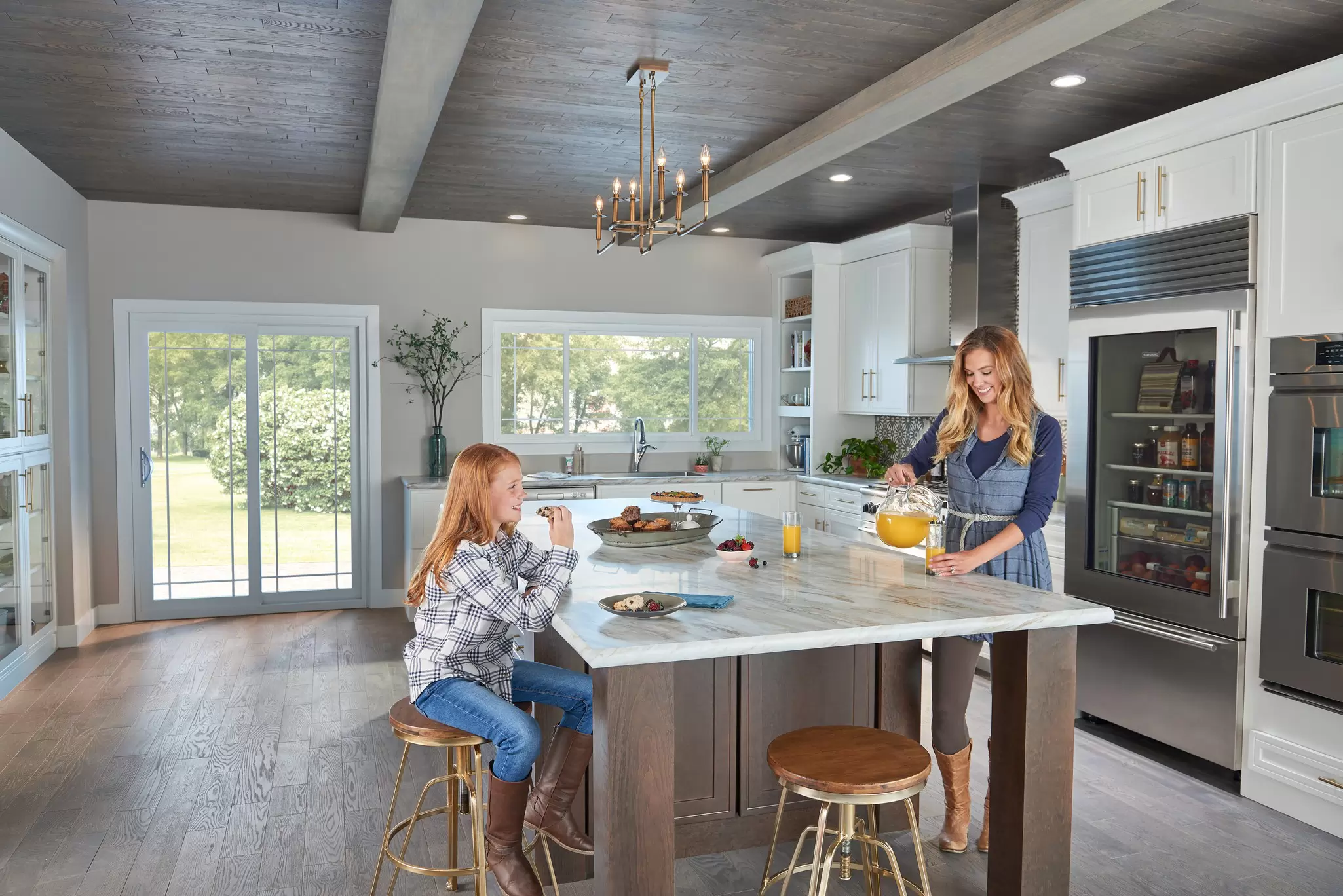 Woman and daughter at a kitchen counter eating snacks and drinking orange juice.