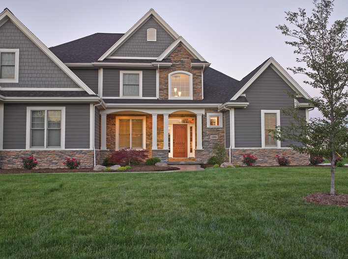 Large gray-colored home with custom windows and a wooden entry door.