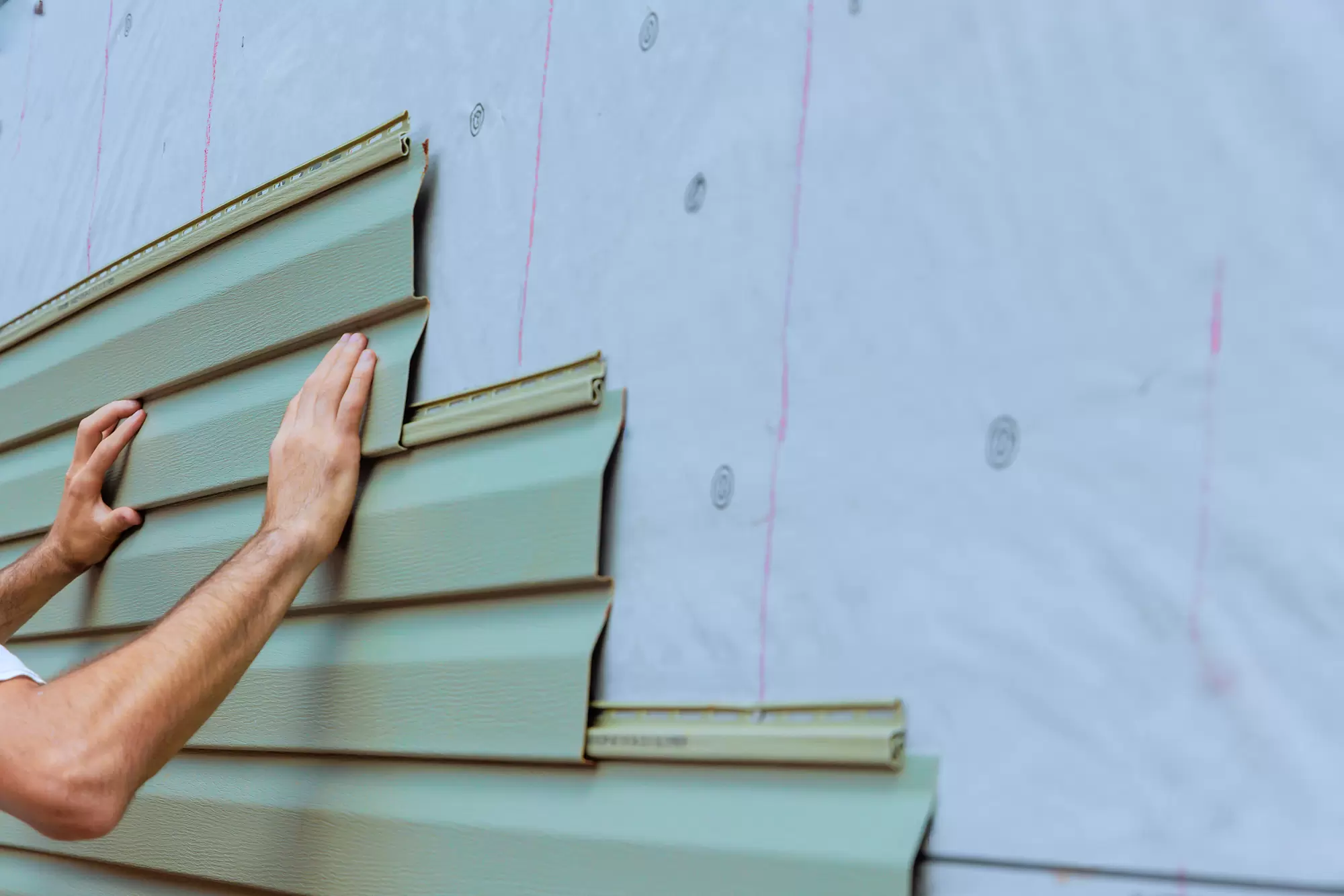 Installer attaching horizontal vinyl siding panels to an exterior wall.