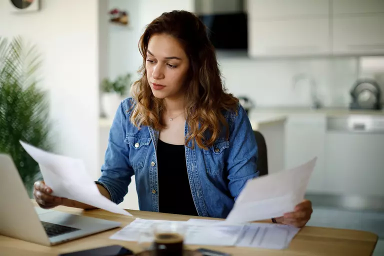 A woman sitting at the table looking at papers and a laptop.