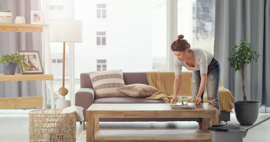 Woman tidying up a living room table with a large picture window in the background 