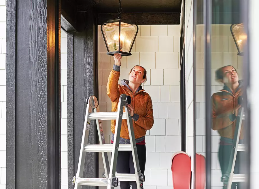 Homeowner standing on a ladder replacing the porch light in her home