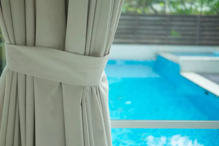 Patio door curtains pulled to the side, showing the home’s large pool and backyard area.