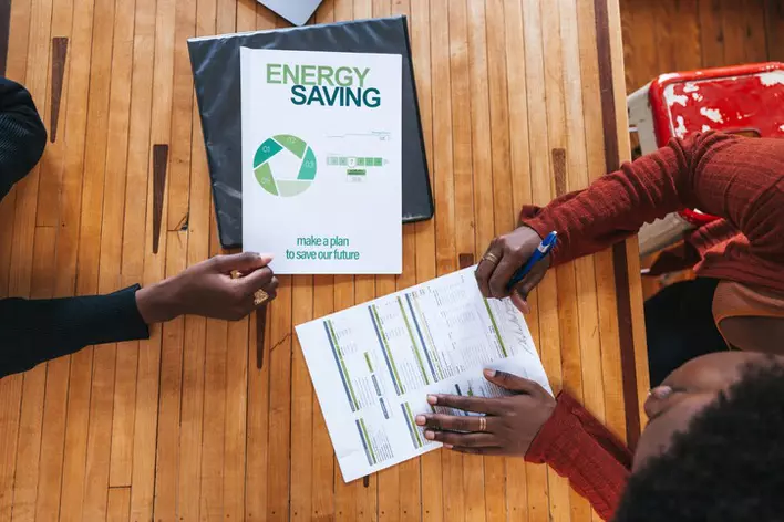 A contractor and a homeowner going over paperwork that outlines the cost reductions the homeowner will benefit from thanks to an energy-saving program.