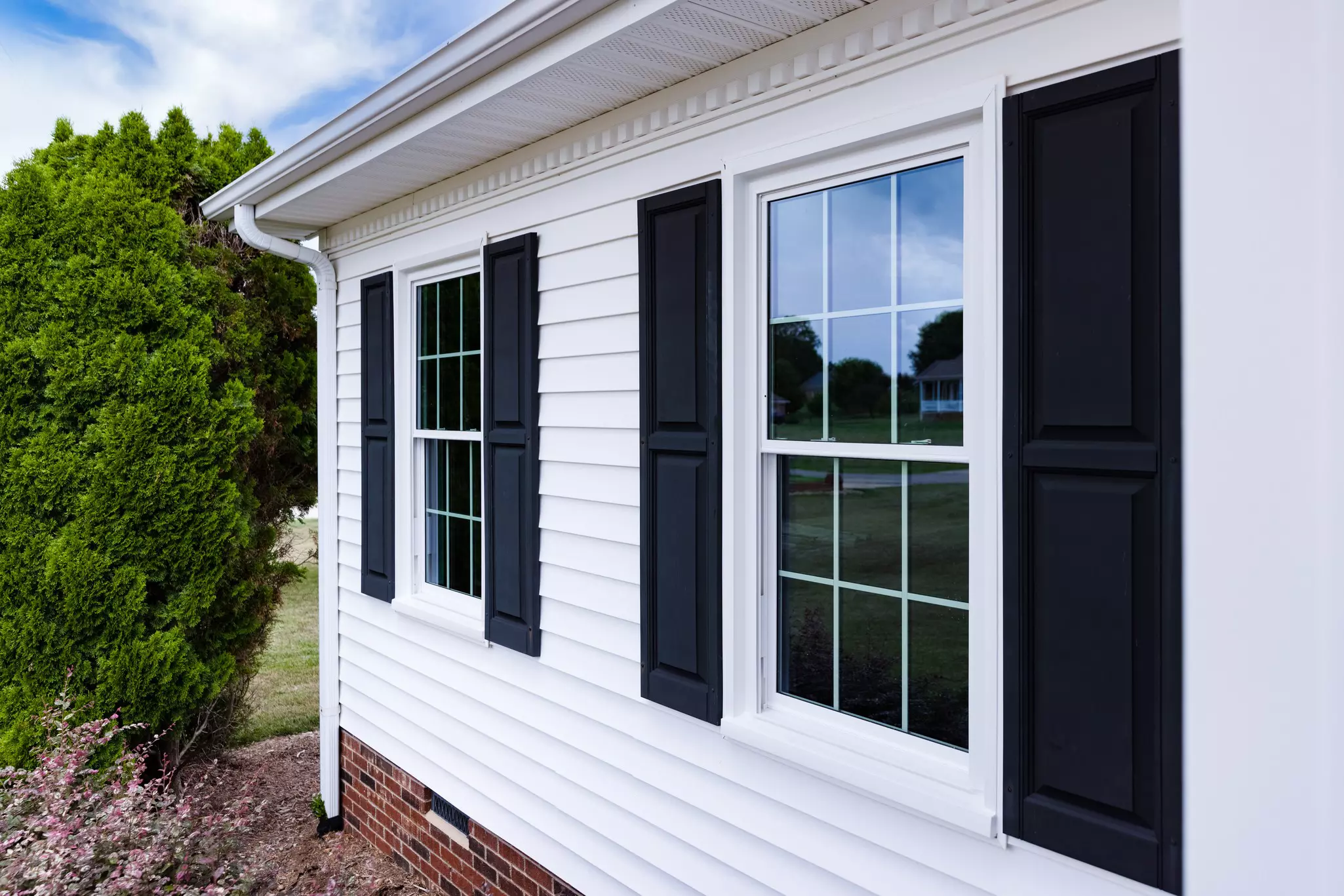 Side of a home with white double-hung windows and black shutters.