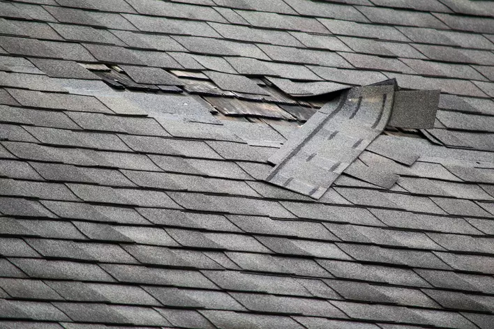 A roof of asphalt shingles that has a section of broken and missing shingles.