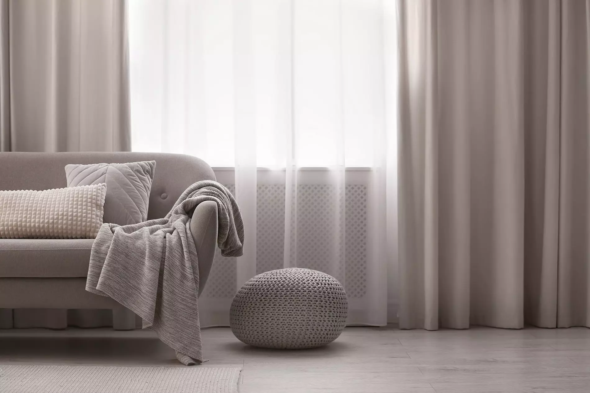 Room containing a couch with pillows on it in front of a window with floor-length drapes.